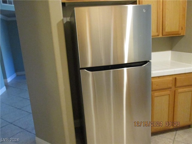 kitchen featuring light brown cabinetry, tile countertops, stainless steel refrigerator, and light tile patterned flooring