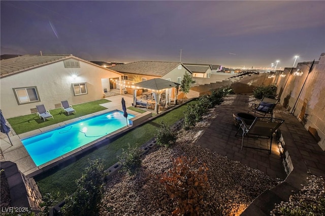 pool at dusk with a gazebo and a patio