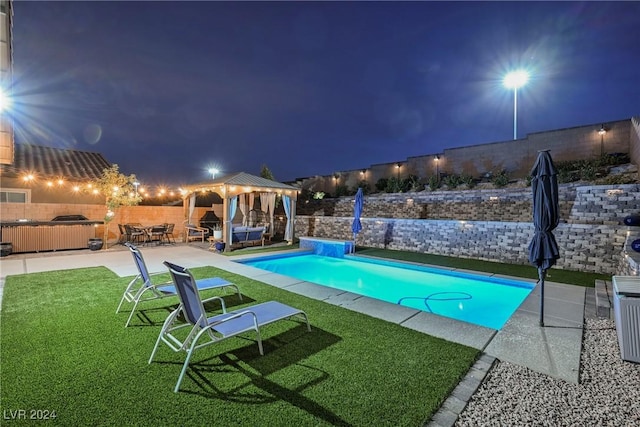 pool at night with a gazebo, a jacuzzi, a lawn, and a patio