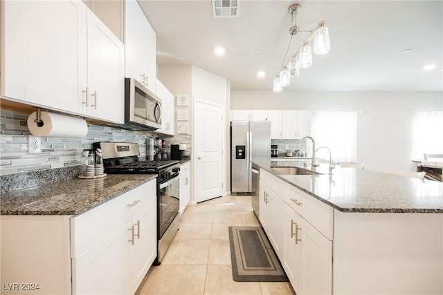 kitchen featuring backsplash, stainless steel appliances, white cabinetry, and an island with sink