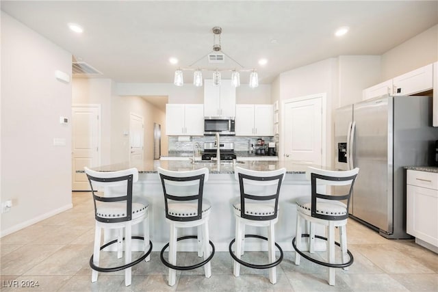 kitchen featuring appliances with stainless steel finishes, backsplash, pendant lighting, a center island with sink, and white cabinets