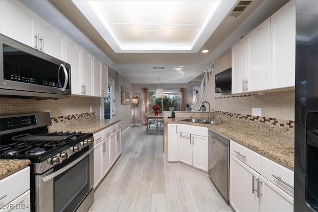 kitchen with sink, white cabinetry, stainless steel appliances, light stone counters, and kitchen peninsula