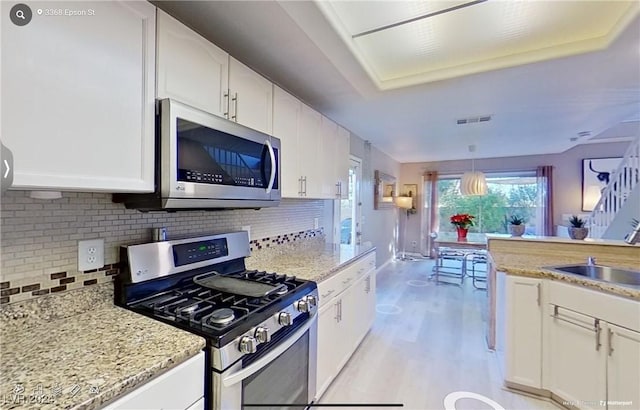 kitchen with sink, light wood-type flooring, appliances with stainless steel finishes, pendant lighting, and white cabinets