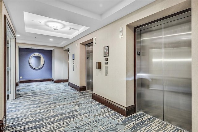 hallway featuring dark colored carpet, elevator, and a raised ceiling