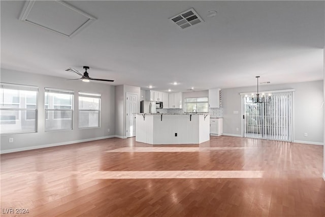 unfurnished living room featuring ceiling fan with notable chandelier and light hardwood / wood-style floors