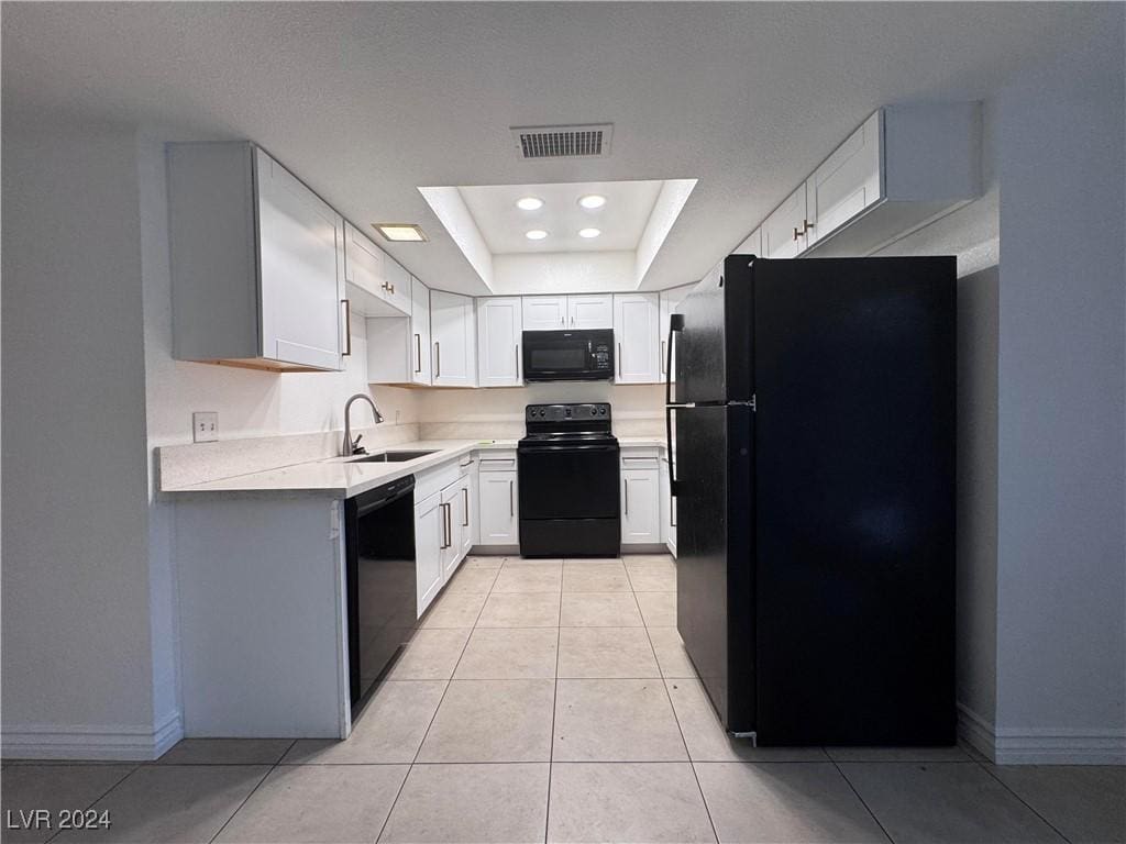 kitchen with black appliances, white cabinets, sink, light tile patterned floors, and a tray ceiling