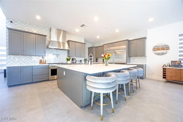 kitchen with a breakfast bar area, gray cabinets, a spacious island, and wall chimney range hood