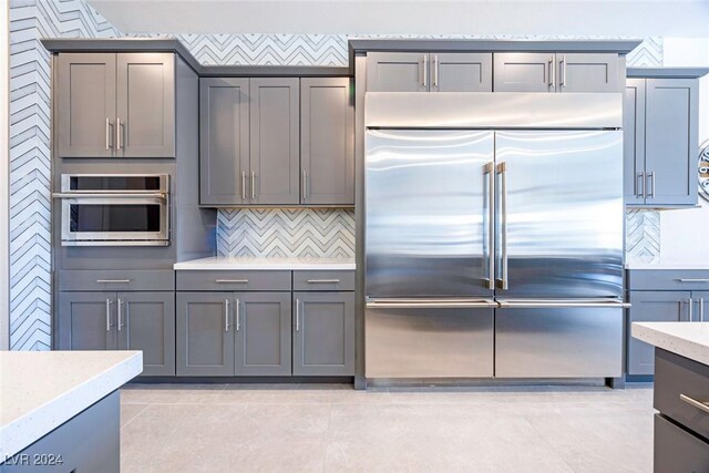 kitchen with backsplash, gray cabinets, light stone counters, and stainless steel appliances