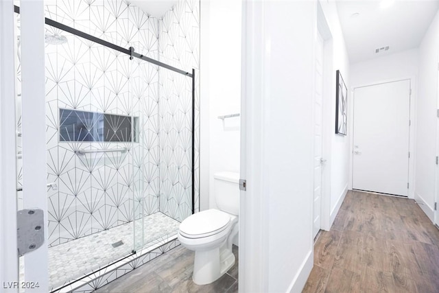 bathroom with hardwood / wood-style floors, toilet, and a shower with door