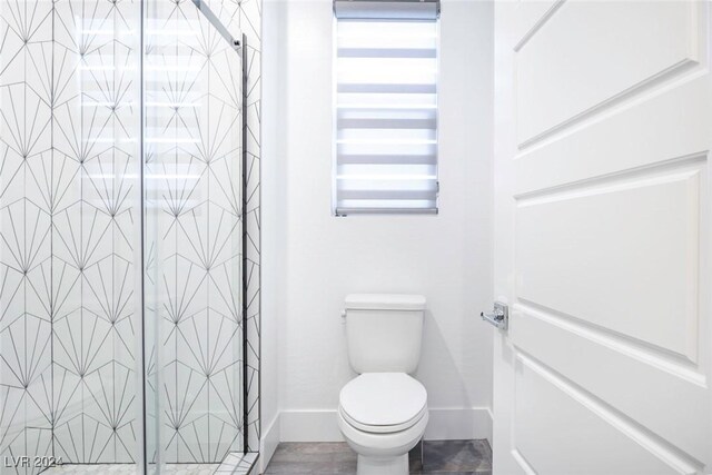 bathroom featuring a shower with door and toilet