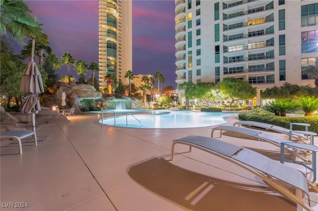 pool at dusk with a patio and pool water feature