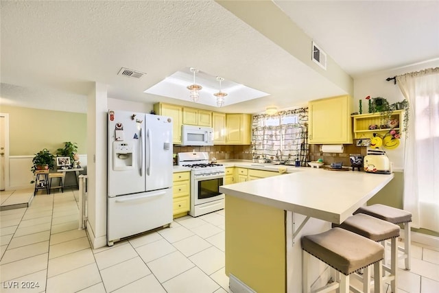 kitchen featuring sink, kitchen peninsula, white appliances, a breakfast bar area, and decorative backsplash