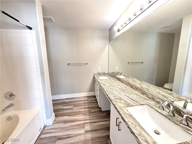 full bathroom featuring wood-type flooring, a textured ceiling, toilet, vanity, and tiled shower / bath