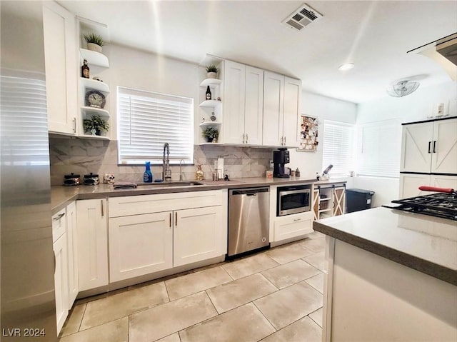 kitchen featuring decorative backsplash, appliances with stainless steel finishes, sink, light tile patterned floors, and white cabinetry