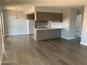 kitchen with sink, dark wood-type flooring, a notable chandelier, white refrigerator, and kitchen peninsula