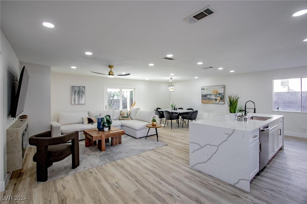 kitchen with dishwasher, white cabinets, a center island with sink, sink, and light wood-type flooring