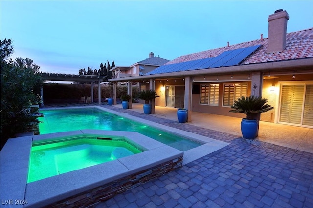 pool at dusk featuring a pergola, an in ground hot tub, and a patio