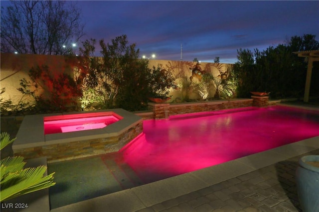 pool at dusk featuring an in ground hot tub