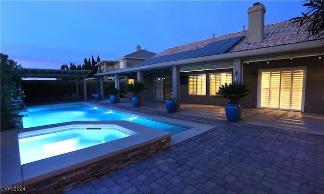 pool at dusk with a pergola, an in ground hot tub, and a patio