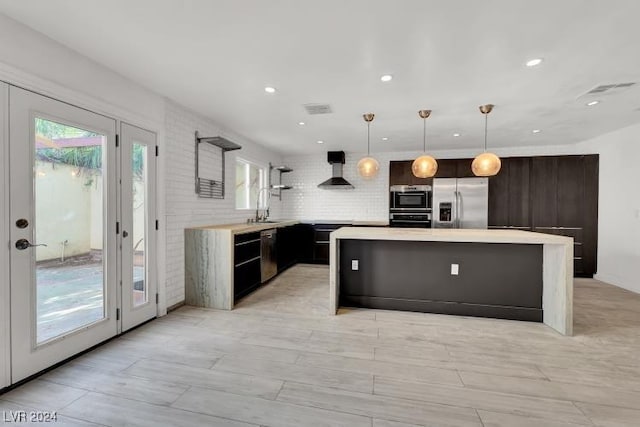 kitchen with decorative light fixtures, a center island, stainless steel appliances, and wall chimney range hood