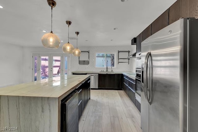 kitchen featuring french doors, light hardwood / wood-style floors, appliances with stainless steel finishes, decorative light fixtures, and a kitchen island