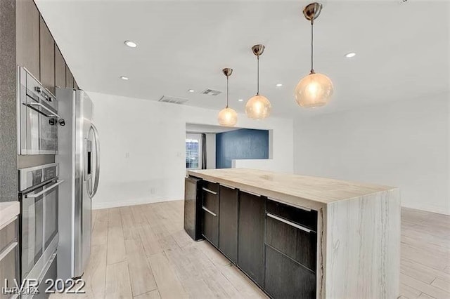 kitchen featuring light wood-type flooring, stainless steel appliances, a kitchen island, and hanging light fixtures