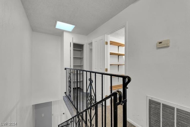 corridor with carpet flooring, a textured ceiling, and a skylight