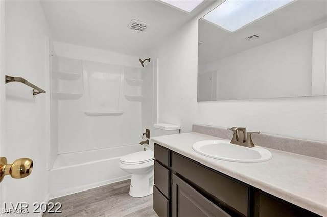 full bathroom featuring hardwood / wood-style floors, vanity,  shower combination, a skylight, and toilet