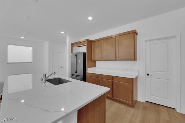 kitchen with light stone countertops, kitchen peninsula, sink, light hardwood / wood-style flooring, and stainless steel refrigerator