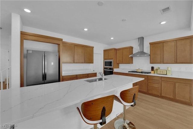 kitchen featuring sink, a breakfast bar area, wall chimney exhaust hood, light hardwood / wood-style floors, and stainless steel appliances