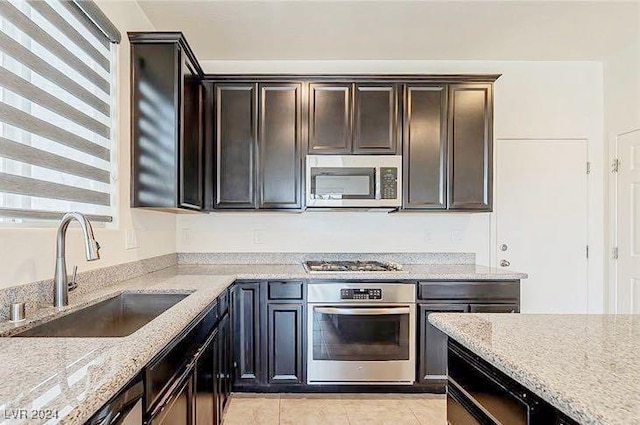 kitchen featuring sink, light tile patterned floors, light stone countertops, appliances with stainless steel finishes, and dark brown cabinetry