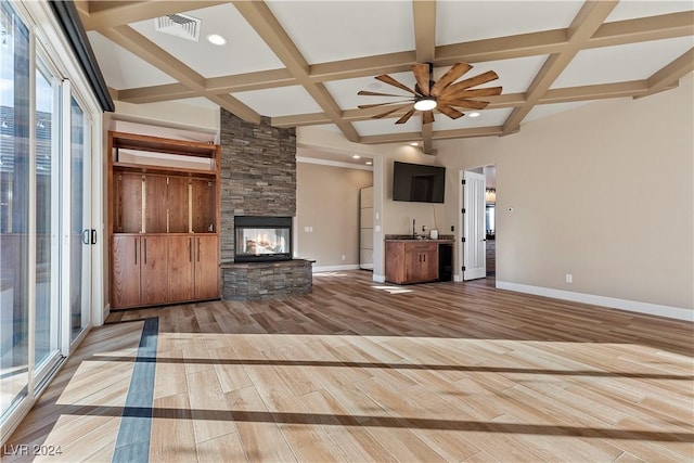 unfurnished living room featuring beamed ceiling, ceiling fan, a fireplace, and light hardwood / wood-style flooring