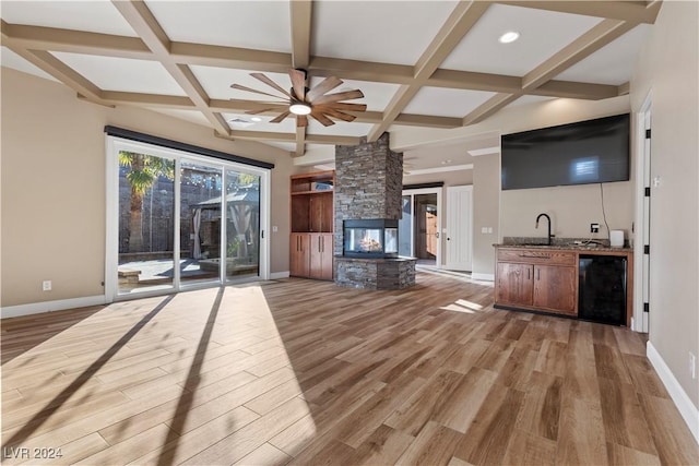 unfurnished living room with a stone fireplace, sink, ceiling fan, beamed ceiling, and light hardwood / wood-style floors