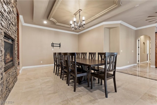 dining room featuring a fireplace, ceiling fan with notable chandelier, a raised ceiling, and crown molding