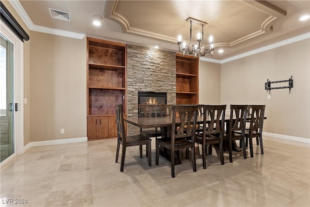 dining room with ornamental molding, a tray ceiling, an inviting chandelier, built in features, and a fireplace