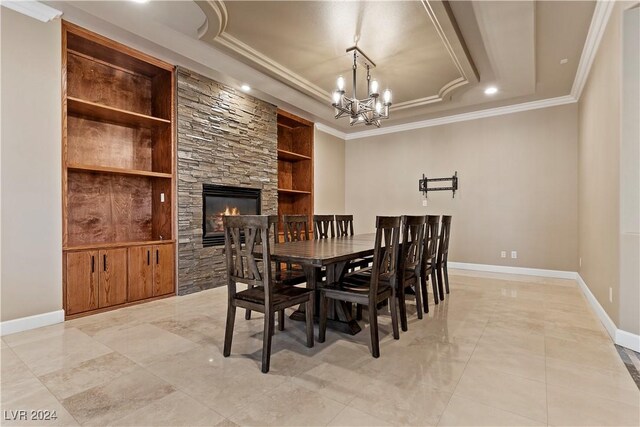 dining space featuring built in features, a chandelier, a tray ceiling, a fireplace, and ornamental molding