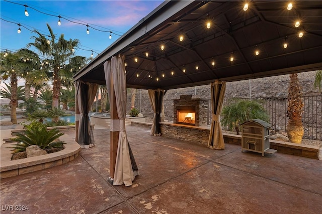 patio terrace at dusk featuring a gazebo and an outdoor stone fireplace