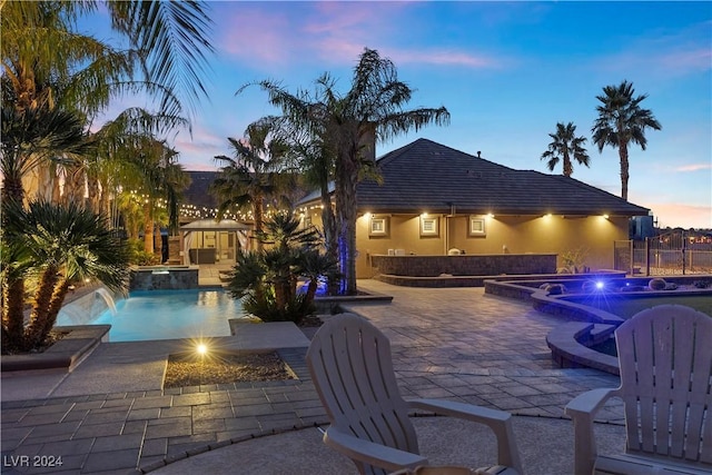 pool at dusk featuring pool water feature, an in ground hot tub, and a patio