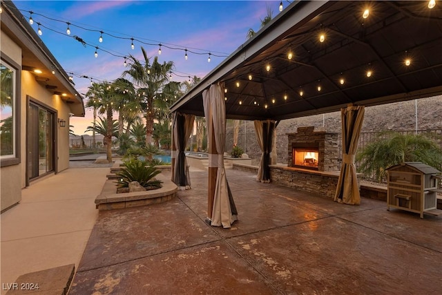 patio terrace at dusk featuring an outdoor stone fireplace and a gazebo