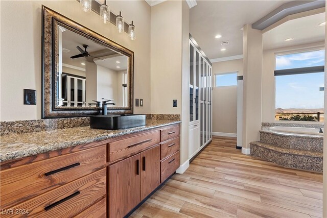 kitchen with light stone counters, ornamental molding, ceiling fan, sink, and light hardwood / wood-style flooring