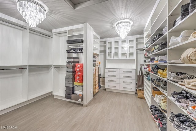 spacious closet featuring light wood-type flooring and an inviting chandelier