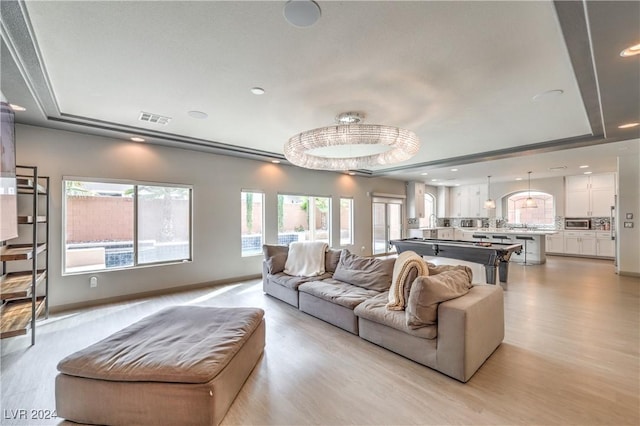 living room with light hardwood / wood-style floors, a raised ceiling, and a notable chandelier