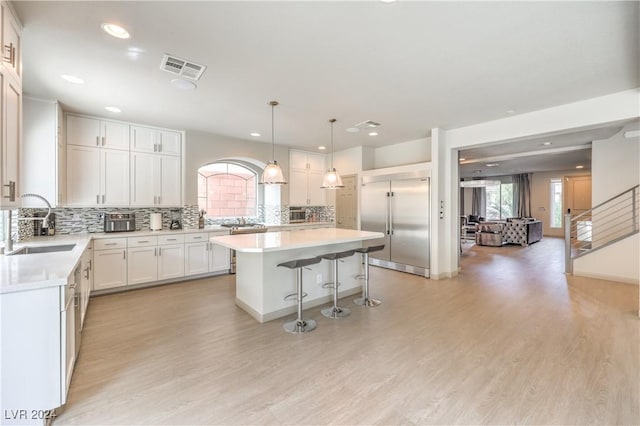 kitchen with white cabinetry, a center island, sink, built in refrigerator, and light wood-type flooring