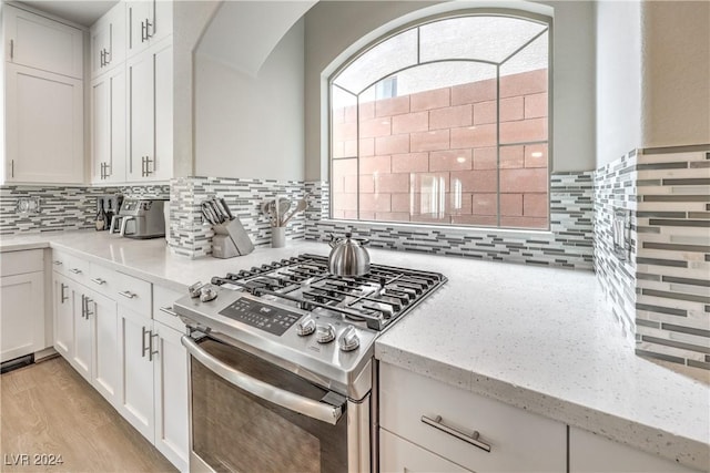 kitchen featuring light stone countertops, tasteful backsplash, light hardwood / wood-style floors, white cabinetry, and stainless steel range with gas stovetop