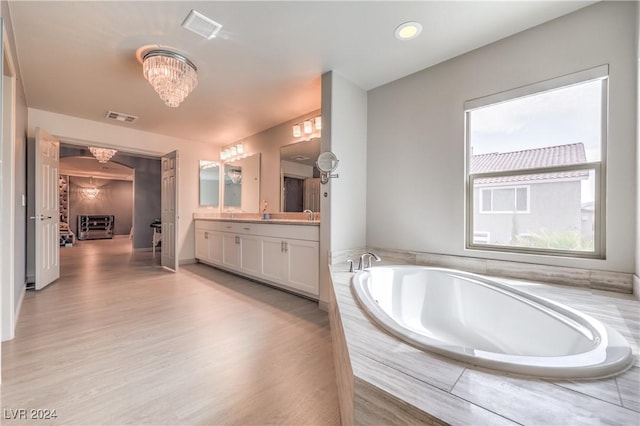 bathroom with vanity, wood-type flooring, tiled tub, and a chandelier