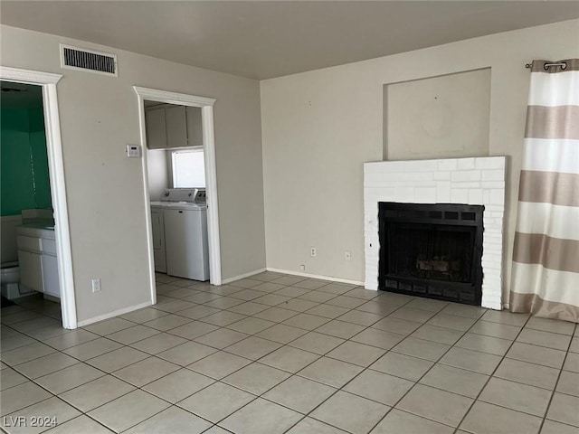 unfurnished living room featuring washing machine and dryer, light tile patterned floors, and a brick fireplace