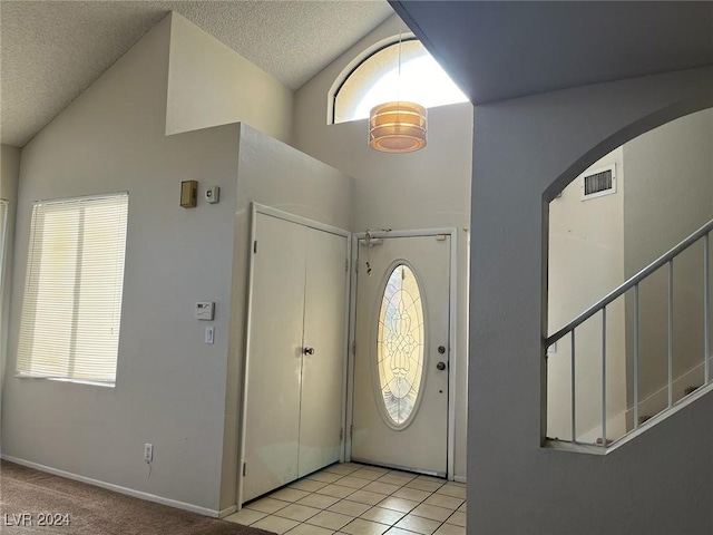 entrance foyer featuring plenty of natural light, light tile patterned floors, a textured ceiling, and high vaulted ceiling