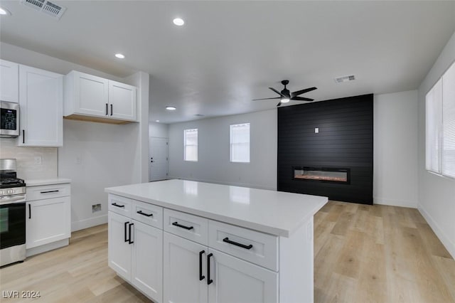 kitchen with appliances with stainless steel finishes, white cabinets, a fireplace, and a wealth of natural light