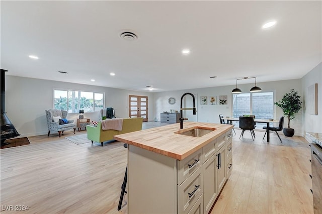 kitchen featuring wood counters, a kitchen island with sink, sink, light hardwood / wood-style flooring, and decorative light fixtures