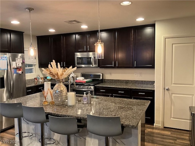 kitchen with pendant lighting, appliances with stainless steel finishes, stone countertops, and a center island with sink